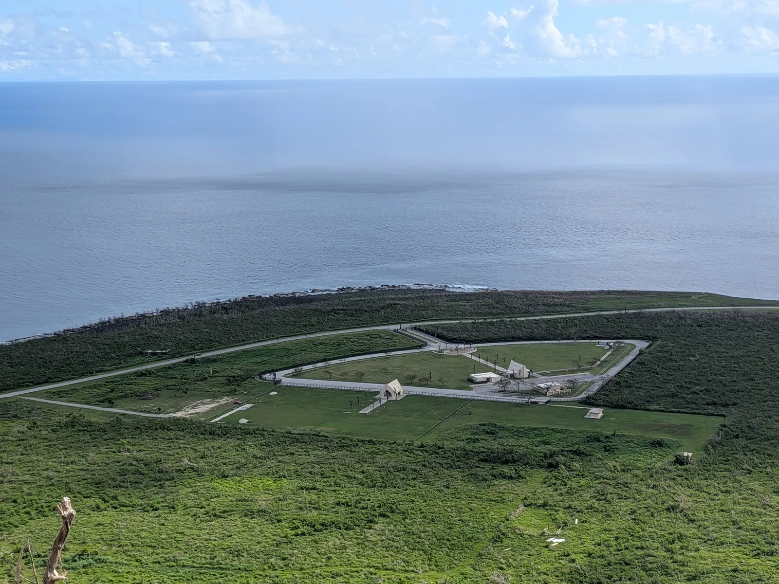 Banzai Cliff's memorial park seen from above at Suicide Cliff, showing its loop road and cluster of monuments on the coastal plain
