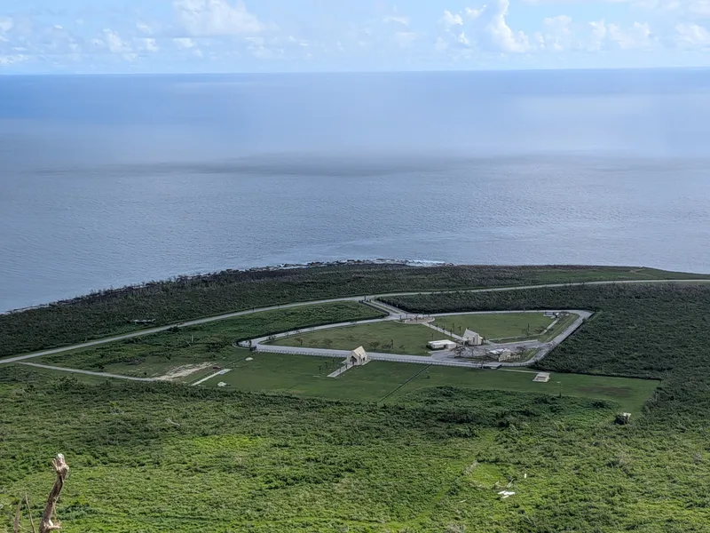 Banzai Cliff's memorial park seen from above at Suicide Cliff, showing its loop road and cluster of monuments on the coastal plain
