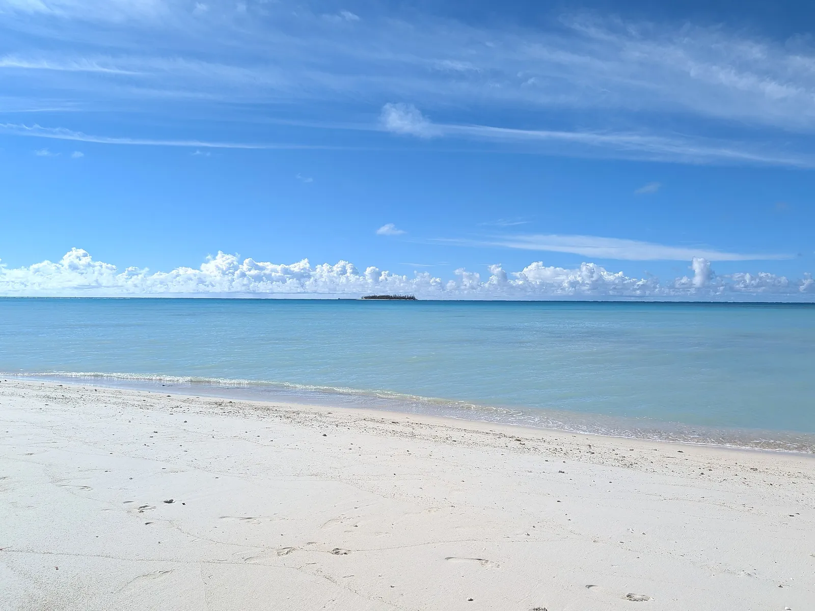 Clear turquoise water and white sand at Micro Beach with a small offshore islet on the horizon