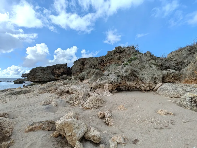 The sand and broken limestone shore at Unai Fanhang, with the headland rising behind