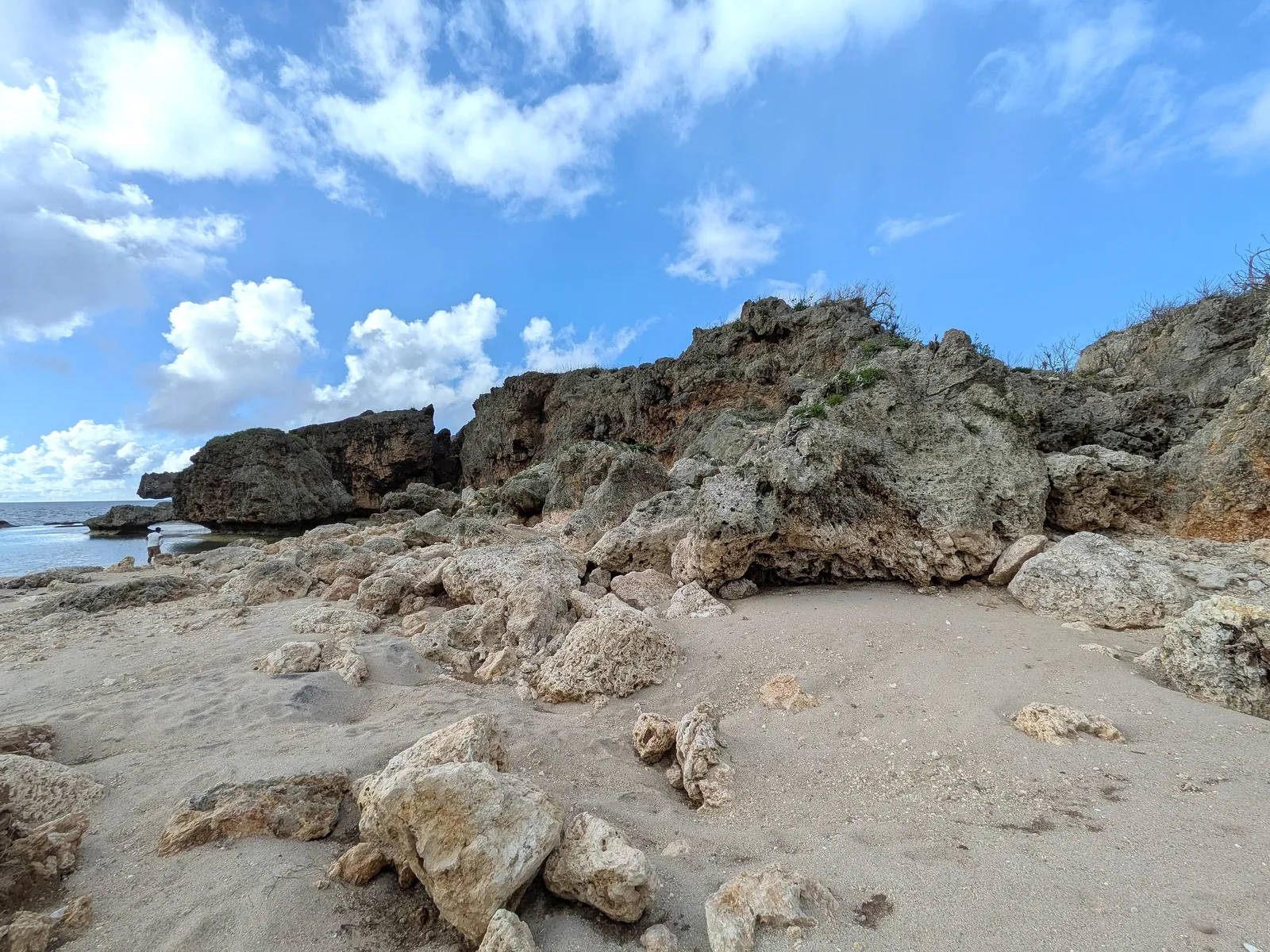 The sand and broken limestone shore at Unai Fanhang, with the headland rising behind