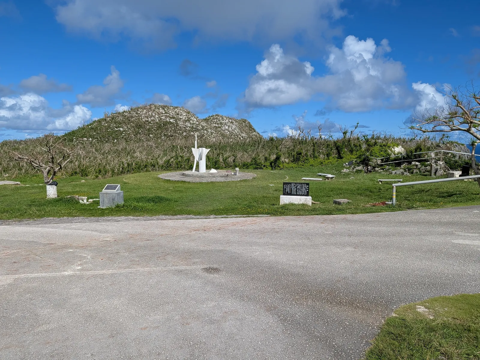 Wide view of the Suicide Cliff memorial complex, showing the peace statue, founding stone, and paved parking loop