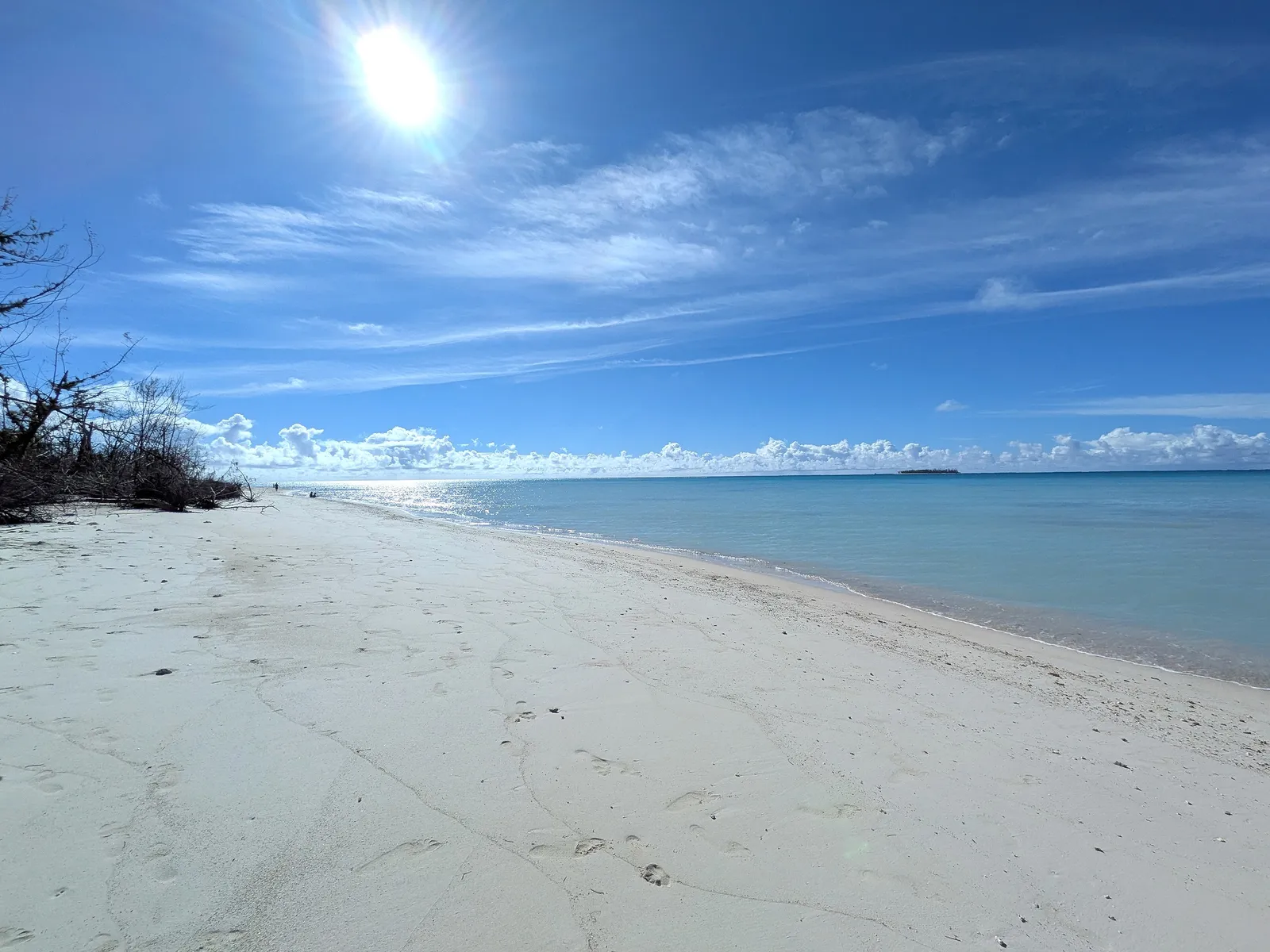 Micro Beach's shoreline looking north, with a few people walking the sand and an offshore islet in the distance