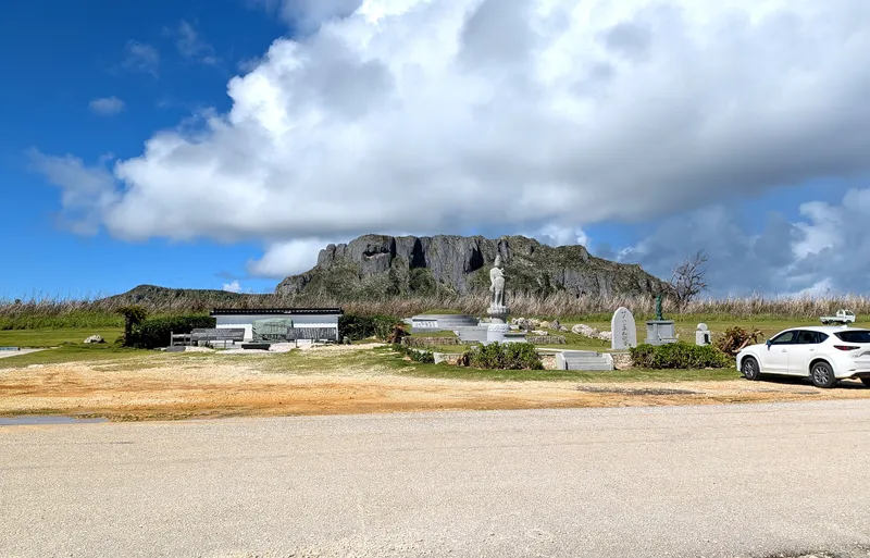 A white Kannon statue in the Banzai Cliff memorial park, with the limestone mass of Suicide Cliff rising inland behind it