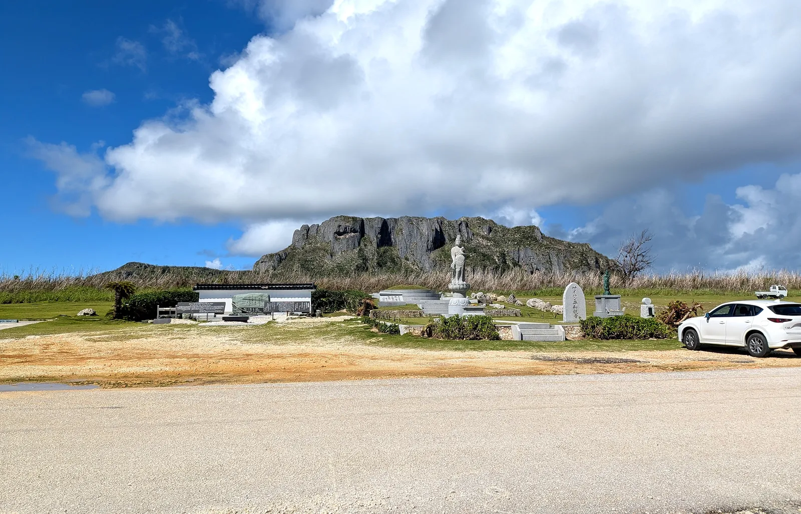 A white Kannon statue in the Banzai Cliff memorial park, with the limestone mass of Suicide Cliff rising inland behind it