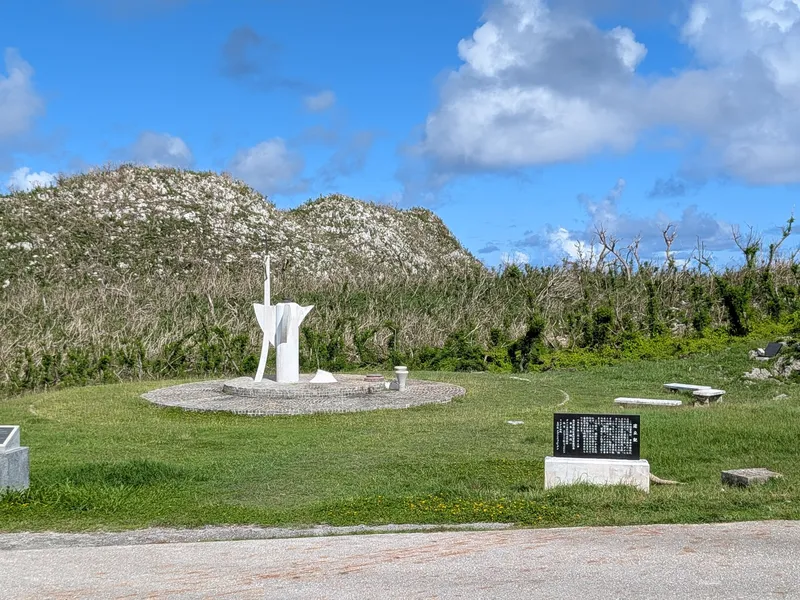 The white peace memorial statue at Suicide Cliff, Saipan, standing on a circular paved base with the limestone rise of Mt. Marpi behind it