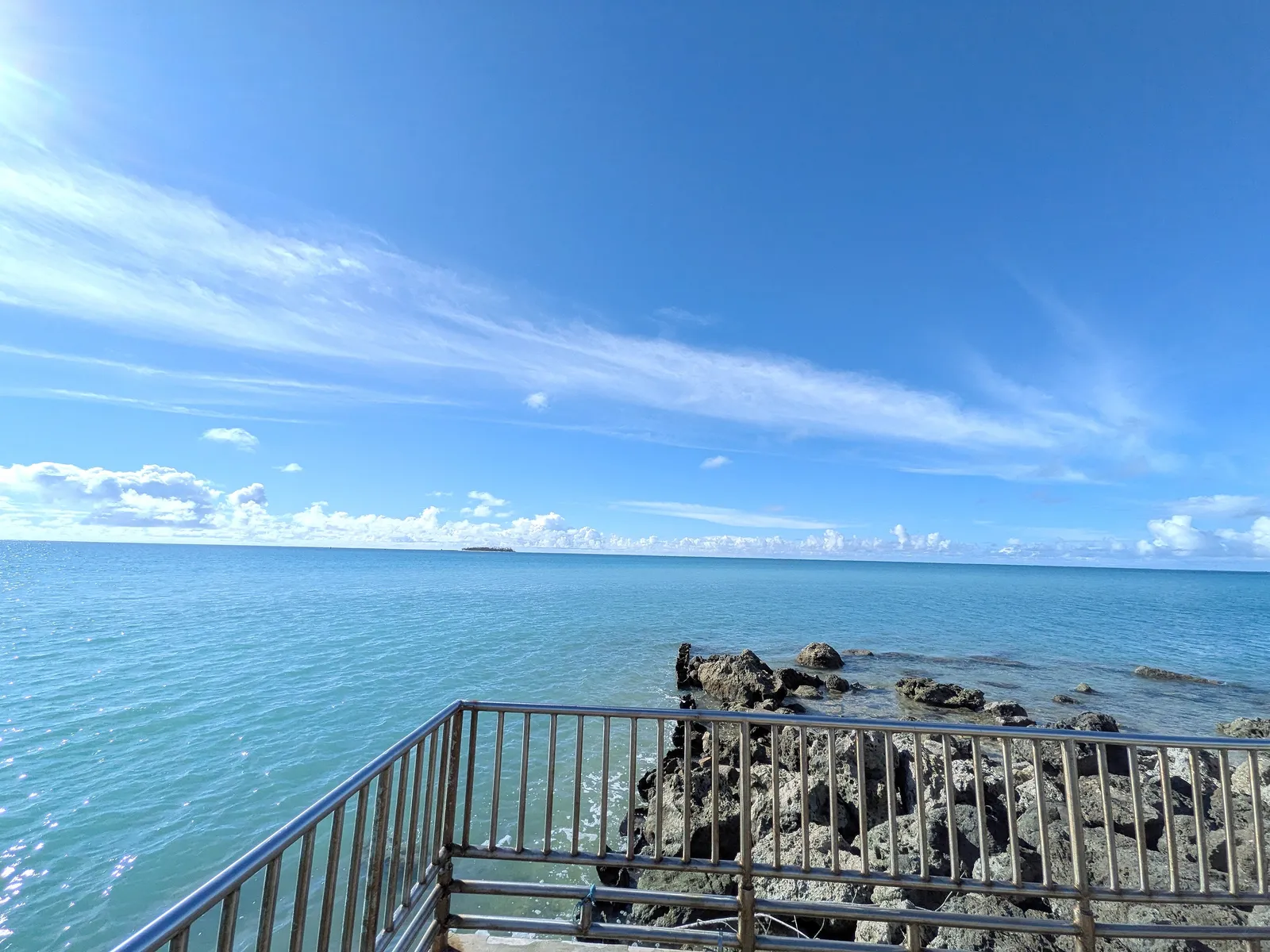 Mañagaha Island on the horizon seen over the seawall railing at Smiling Cove Marina