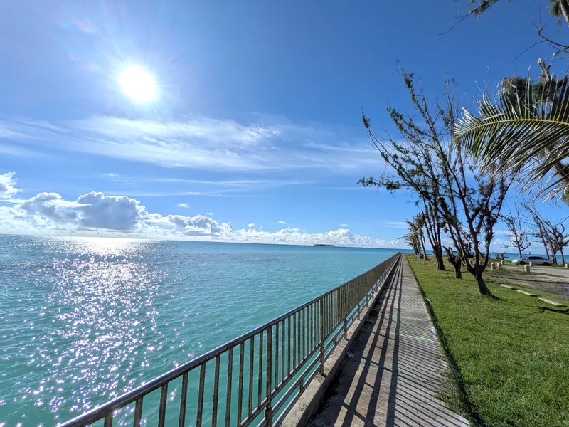 The seawall walking path at Smiling Cove Marina, Saipan, with turquoise lagoon water on one side and Mañagaha visible on the horizon