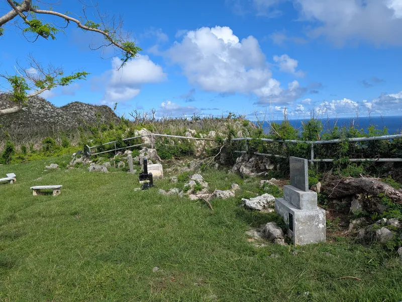 Smaller cenotaphs and grave markers on the grass at Suicide Cliff, with the ocean visible beyond the clifftop railing