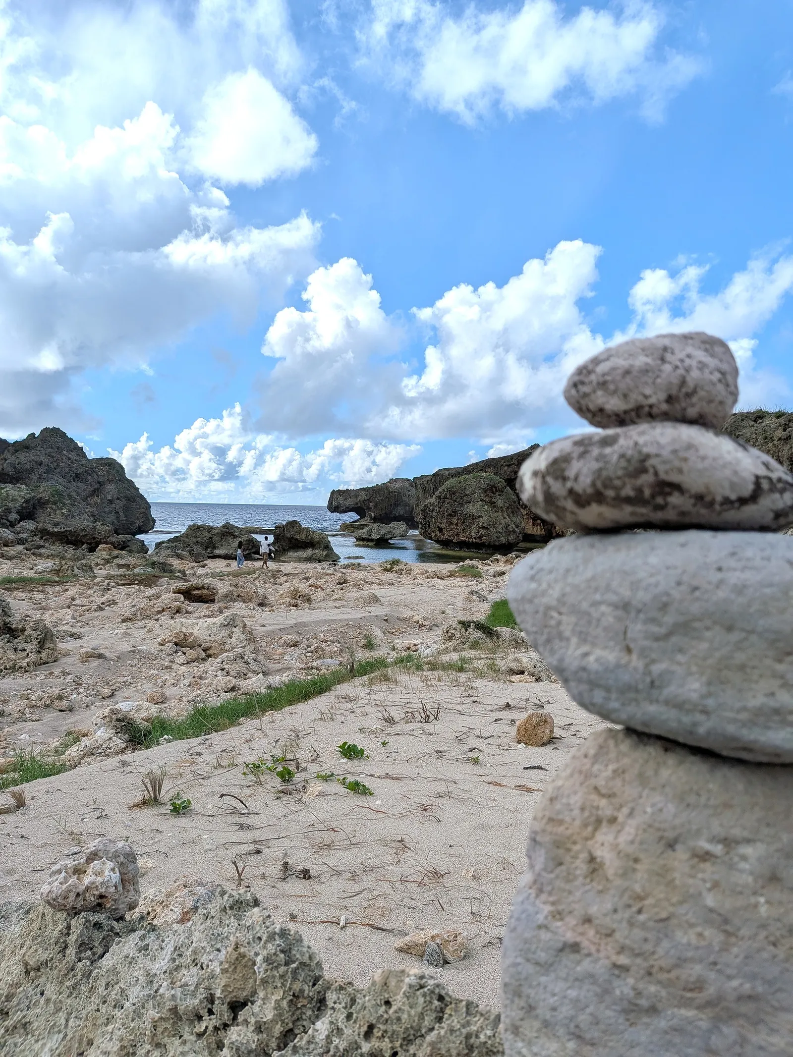 A stack of balanced stones on the shore at Unai Fanhang, with the rock formations and sea beyond