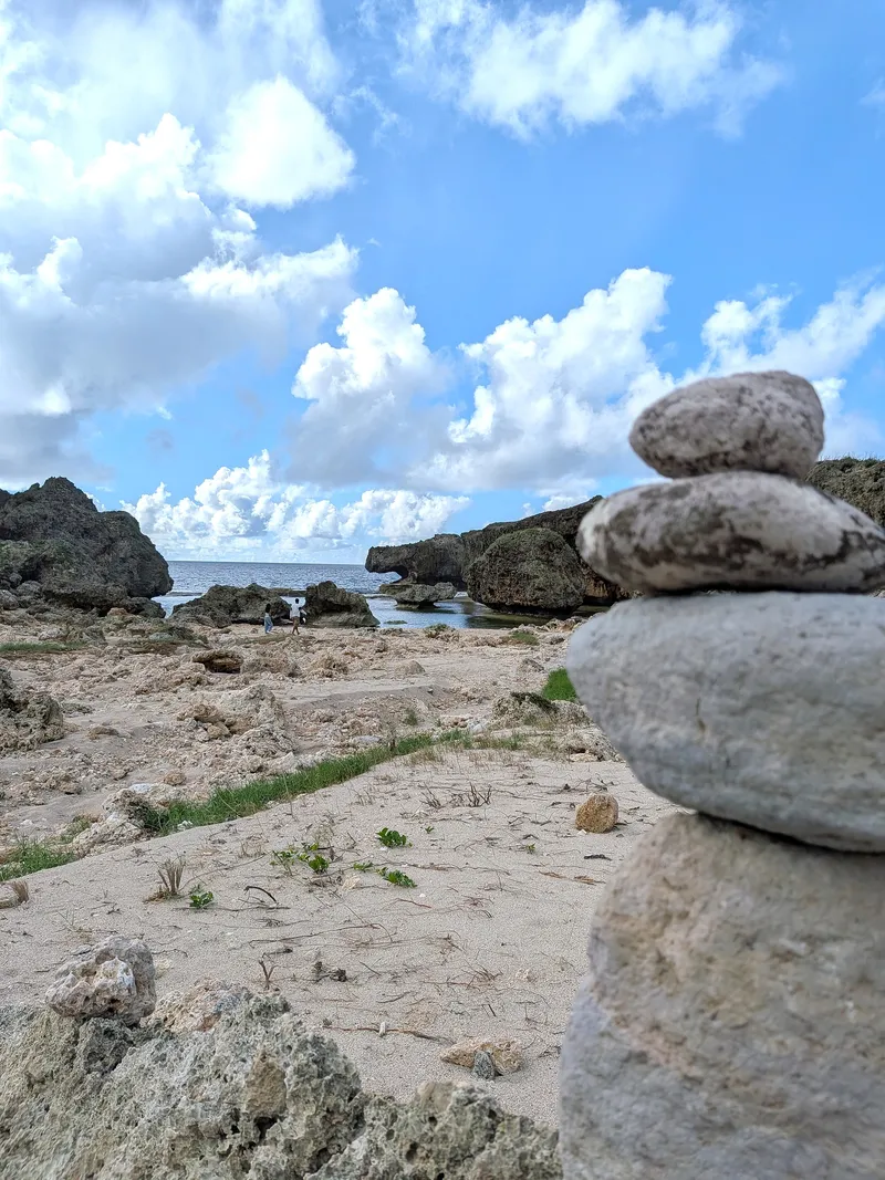 A stack of balanced stones on the shore at Unai Fanhang, with the rock formations and sea beyond