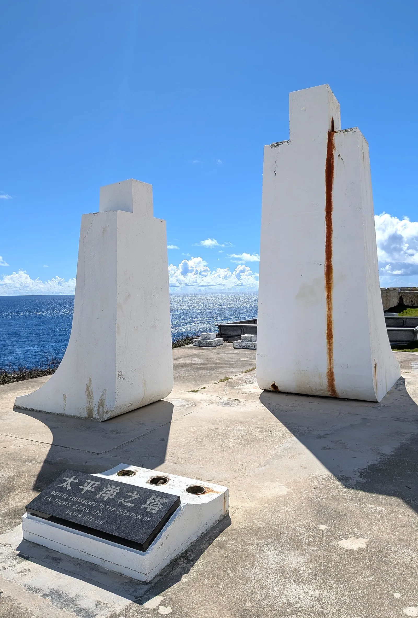 The two white pylons of the Tower of the Pacific at Banzai Cliff, with its dedication plaque reading "Devote yourselves to the creation of the Pacific global era, March 1970"