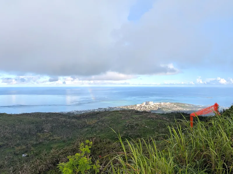 A wide view from Mount Tapochau's lower slopes with a faint rainbow over the coastal plain