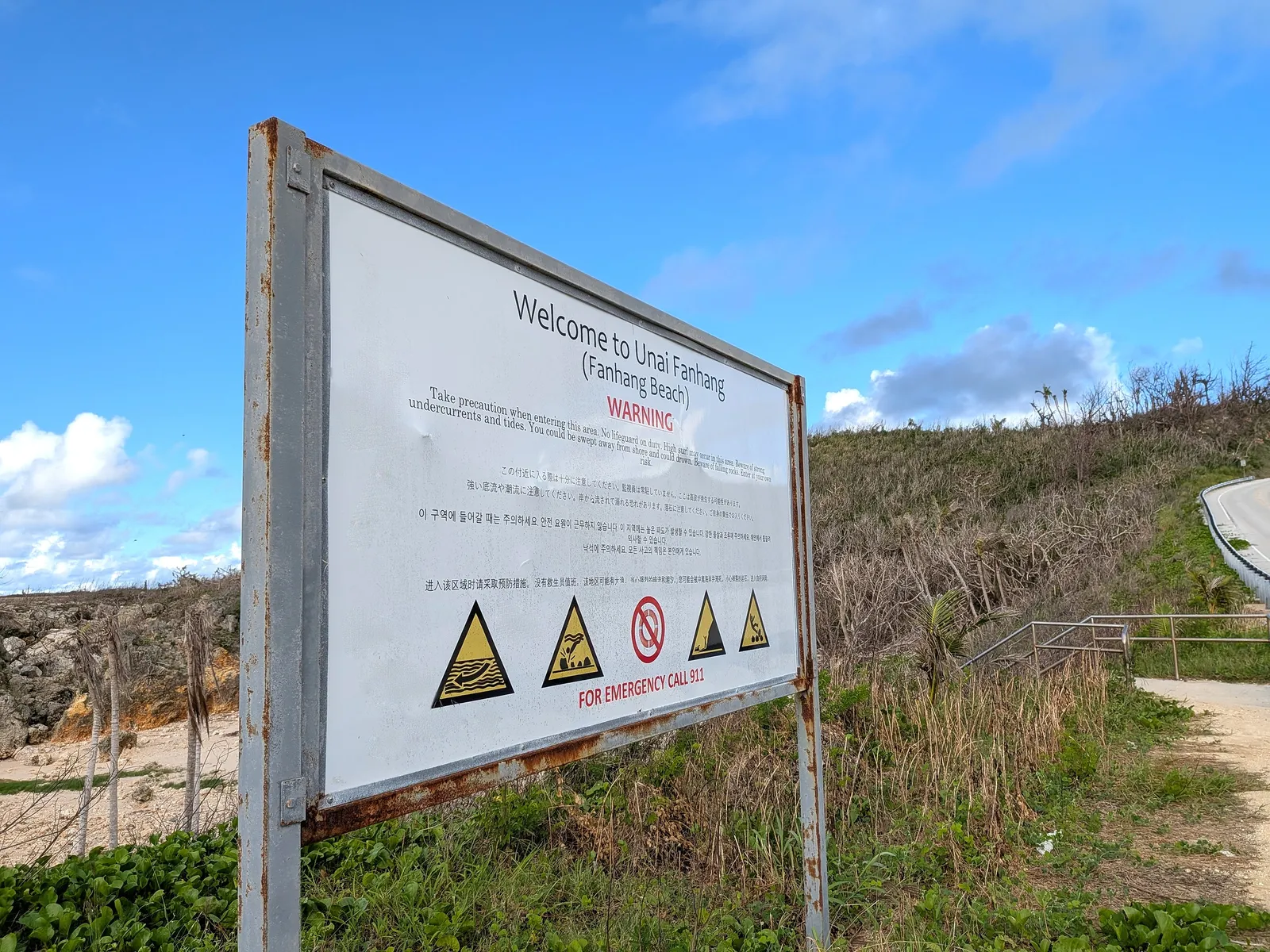The multilingual warning sign at the entrance to Unai Fanhang, listing strong undercurrents, high surf, falling rocks and no lifeguard on duty