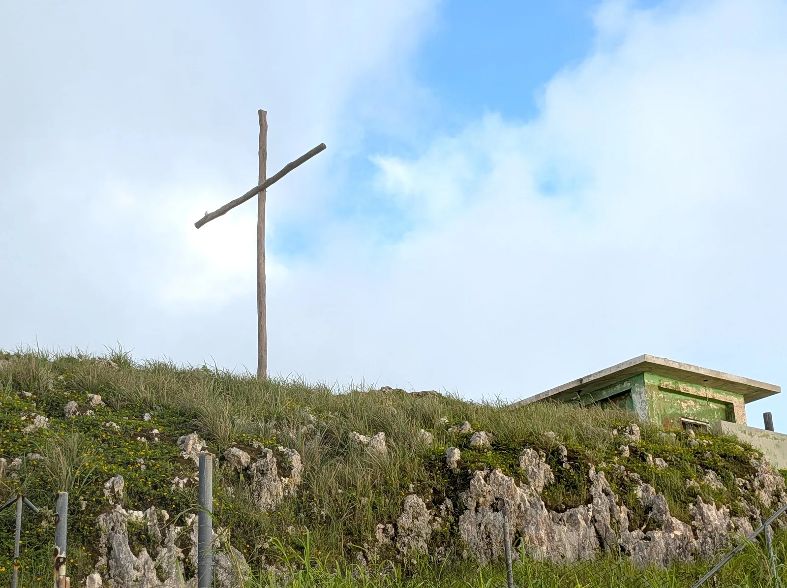 A wooden cross and a small green concrete structure on a side peak near the Mount Tapochau summit